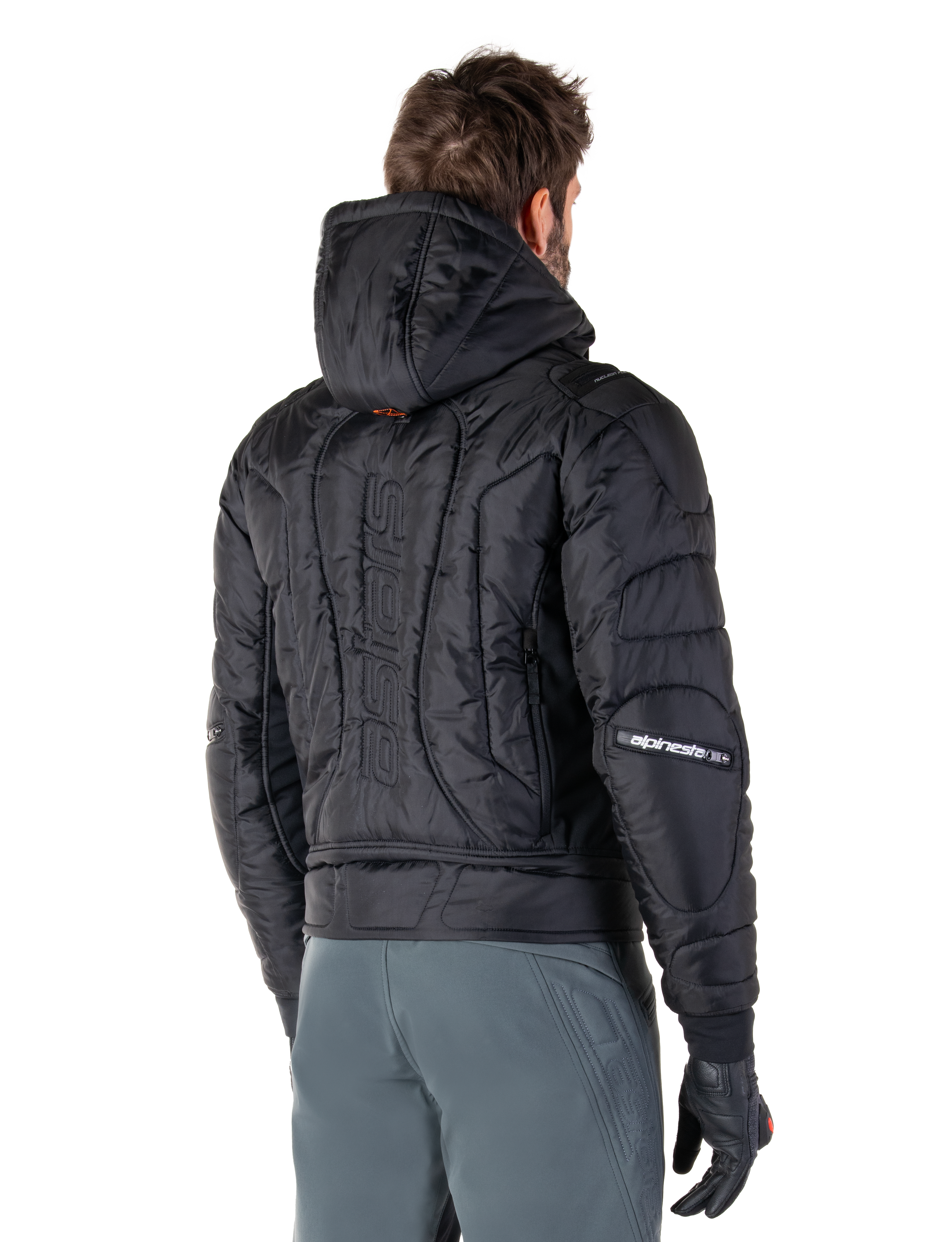 Alpinestars Mohobbs Waterproof Jacket, svart, vy bakifrån som visar quiltad vadderad konstruktion, huva, vertikalt astars-ordmärke på ryggen och Alpinestars-logotyper på ärmarna, bärs med gråa byxor och svarta handskar.