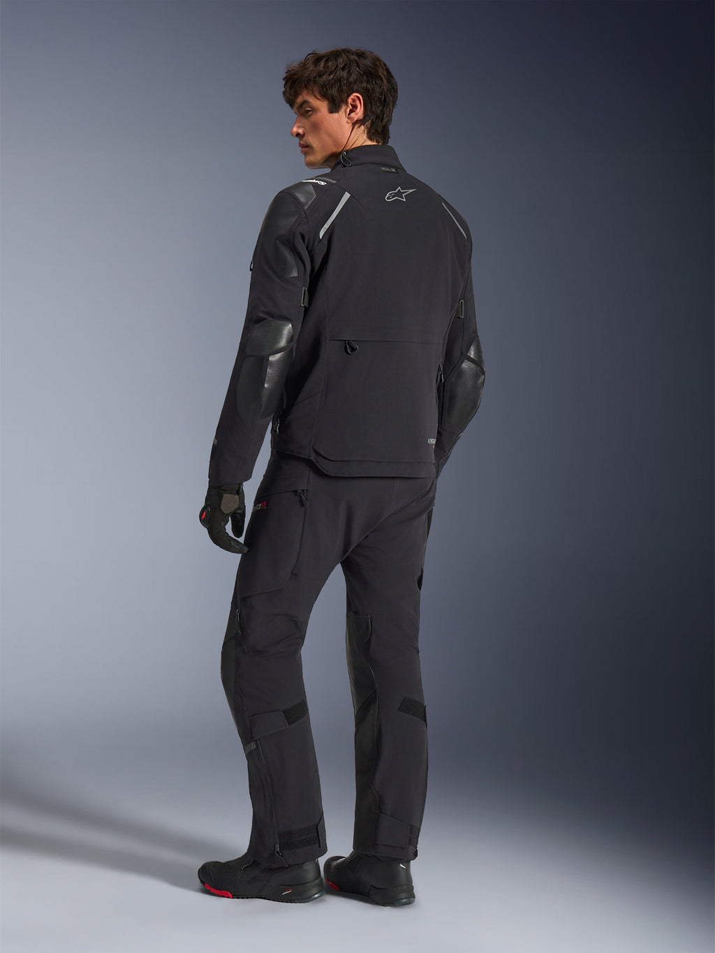 Alpinestars Andes Pro Drystar® XF-jacka, äventyrsmotorcykeljacka, svart, vy bakifrån buren med matchande byxor och stövlar, med förstärkta paneler och silverfärgad stjärnlogotyp, teknisk körutrustning för alla väder