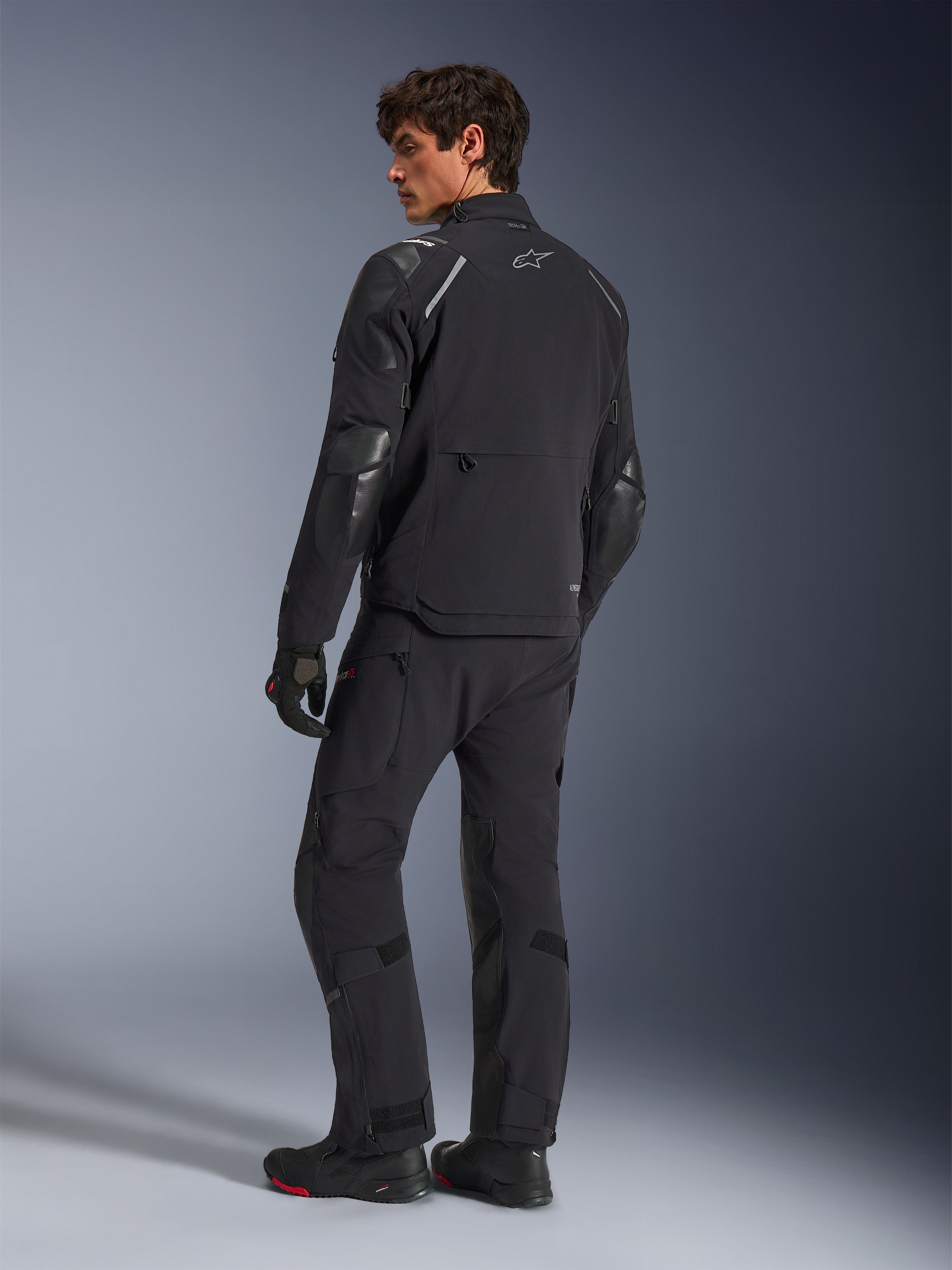 Alpinestars Andes Pro Drystar® XF-jacka, äventyrsmotorcykeljacka, svart, vy bakifrån buren med matchande byxor och stövlar, med förstärkta paneler och silverfärgad stjärnlogotyp, teknisk körutrustning för alla väder