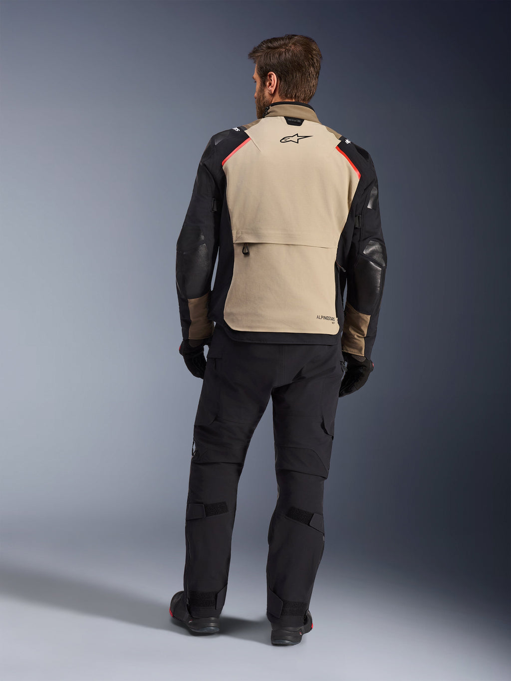Alpinestars Andes Pro Drystar® XF-jacka, Walnut Aluminum, vy bakifrån, adventure-motorcykeljacka med svarta ärmar och röda axeldetaljer, bärs med svarta MC-byxor och handskar