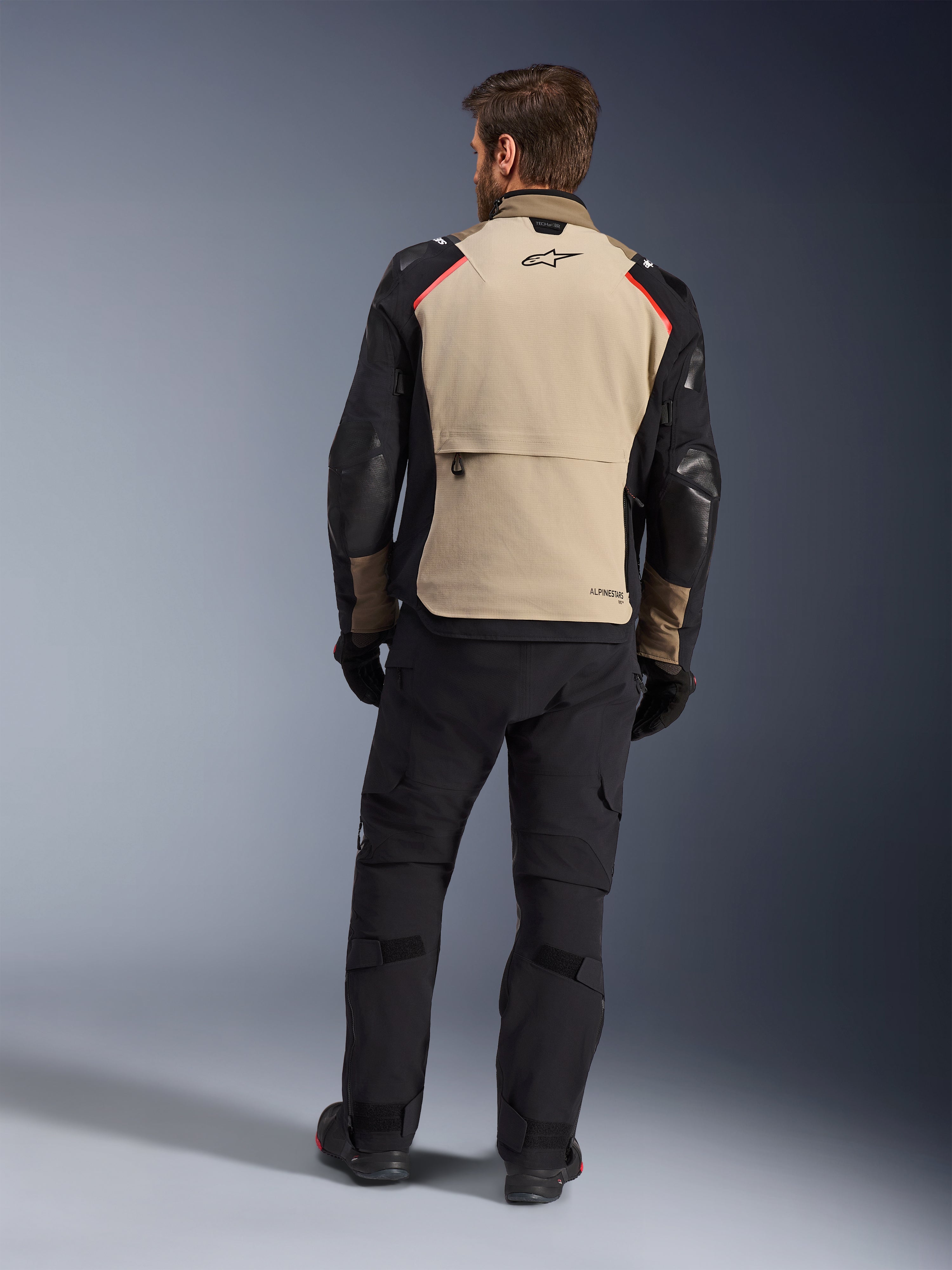 Alpinestars Andes Pro Drystar® XF-jacka, Walnut Aluminum, vy bakifrån, adventure-motorcykeljacka med svarta ärmar och röda axeldetaljer, bärs med svarta MC-byxor och handskar