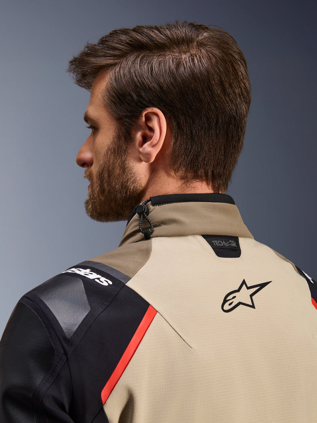 Alpinestars Andes Pro Drystar® XF-jacka i Walnut Aluminum, närbild bakifrån som visar kragen och de övre axlarna, med Alpinestars-logotypen, märkning för Tech-Air-kompatibilitet, röda detaljer och ett justeringssystem med stötsnöre vid nacken.