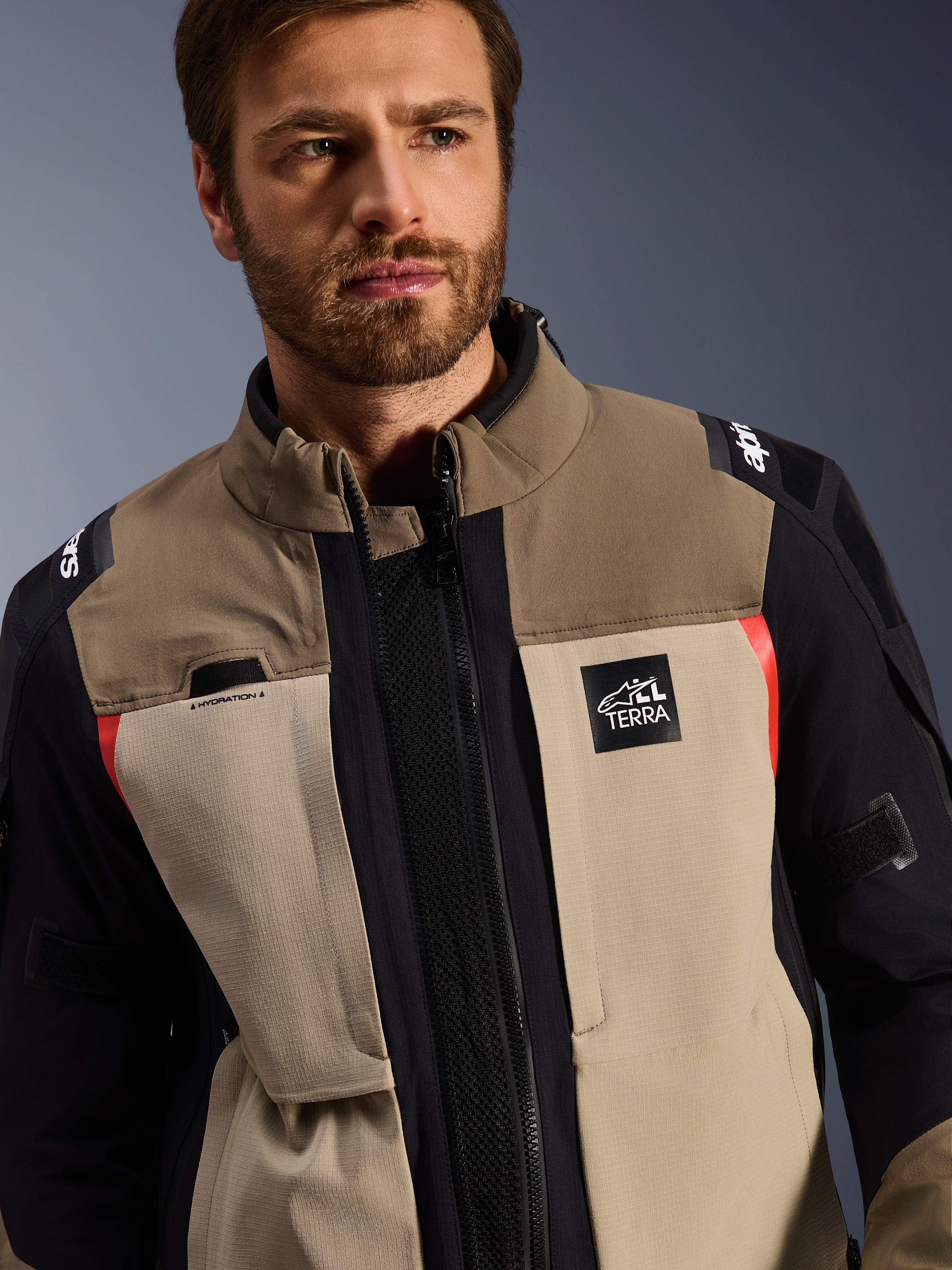 Alpinestars Andes Pro Drystar® XF-jacka i Walnut Aluminum, buren av en manlig modell, äventyrsmotorcykeljacka med en design i flera lager textil i brunt, ljusgrått och svart med röda accenter, Alpinestars 'TERRA'-logotyp på bröstet och synliga tekniska detaljer.