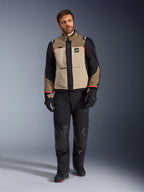 Manlig modell som bär Alpinestars Andes Pro Drystar® XF-jacka i Walnut Aluminum, sandfärgad och svart adventure touring-jacka med röda detaljer, matchad med svarta motorcykelbyxor, handskar och stövlar, helkroppsbild i studio för skyddande körutrustning.