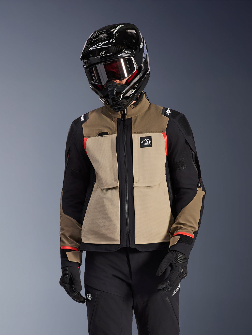 Alpinestars Andes Pro Drystar® XF jacka, adventure touring-motorcykeljacka, Walnut Aluminum i beige och brunt med svarta paneler och röda detaljer, bärs med en svart Alpinestars-hjälm och goggles, teknisk motorcykelutrustning