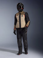 Alpinestars Andes Pro Drystar® XF-jacka i Walnut Aluminum, äventyrsmotorcykeljacka buren med matchande svarta byxor, en svart äventyrshjälm med goggles och svarta stövlar, med beigea och svarta paneler och röda detaljer.
