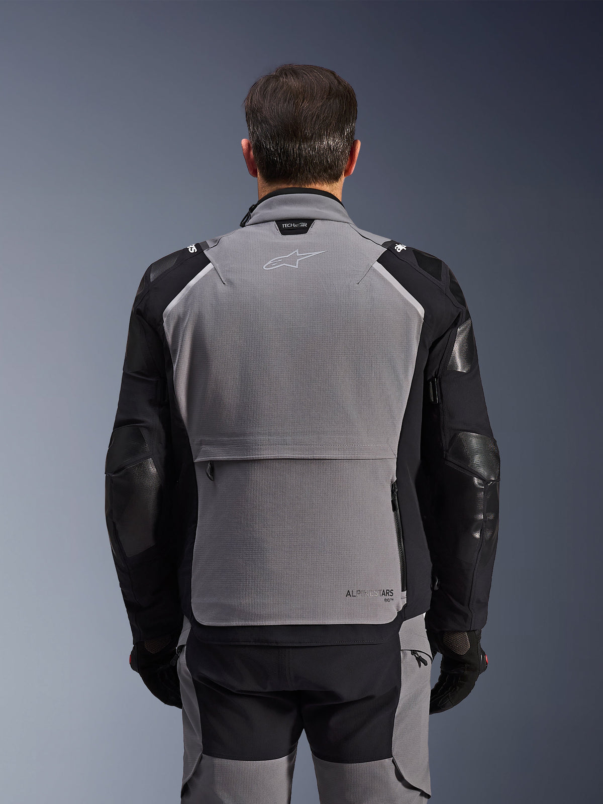 Alpinestars Andes Pro Drystar® XF-jacka, sedd bakifrån, mörkgrå och svart, adventure touring-jacka med en stor bakre förvaringsficka, Tech-Air® Ready-märkning på kragen och förstärkta armbågspaneler.