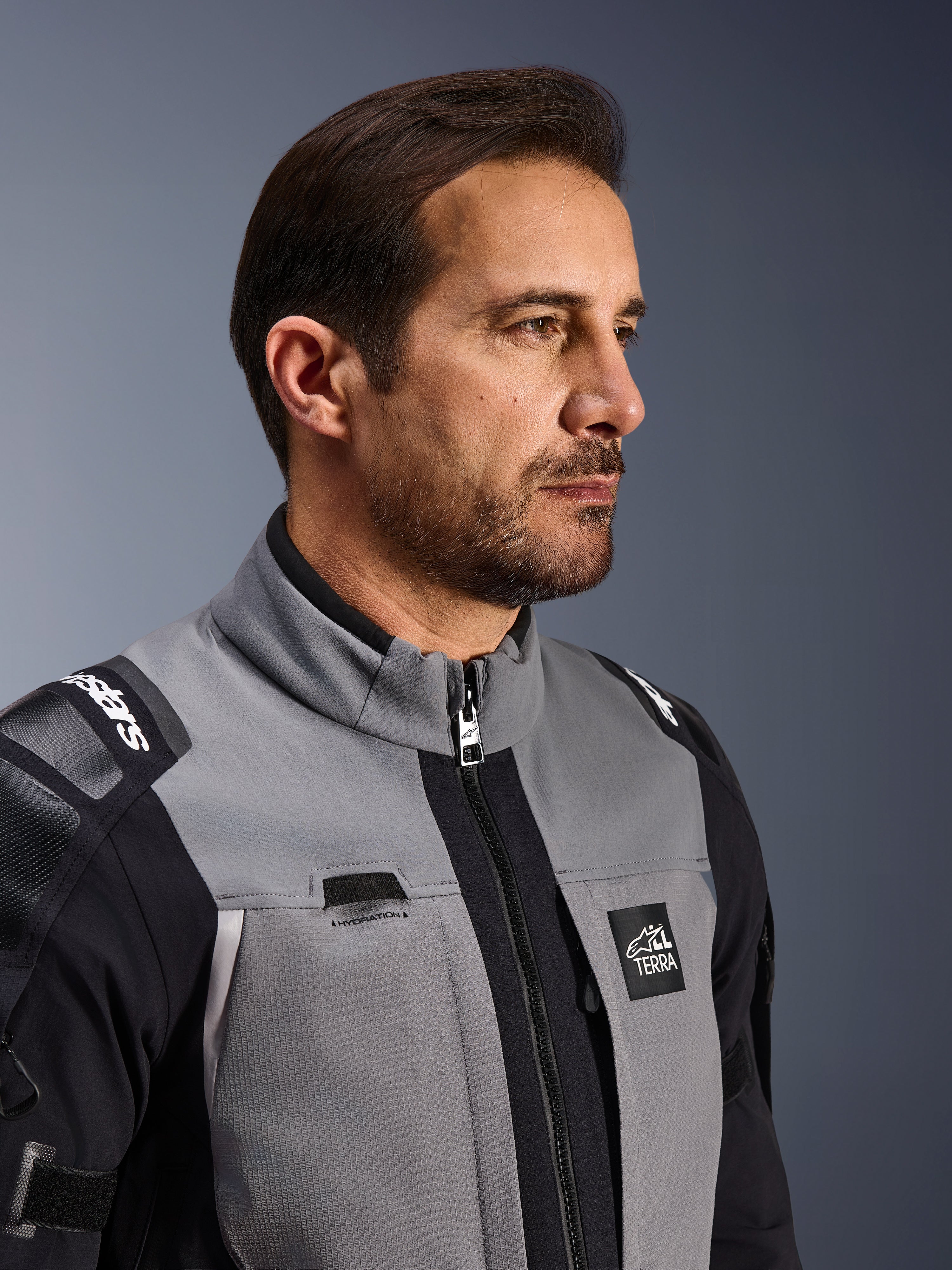 Alpinestars Andes Pro Drystar® XF-jacka, äventyrsjacka för motorcykel, mörkgrå och svart, närbild på bröstparti och krage, med Terra-branding och detalj för vätskerörsledning, bärs av en man i studiomiljö