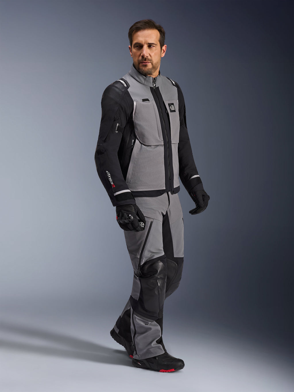 Alpinestars Andes Pro Drystar® XF-jacka, äventyrsmotorcykeljacka, mörkgrå och svart, bärs av en modell med matchande textilbyxor och svarta handskar, design med flera fickor, tekniskt 3-lagers laminerat skal och artikulerad passform för långdistansäventyrskörning.