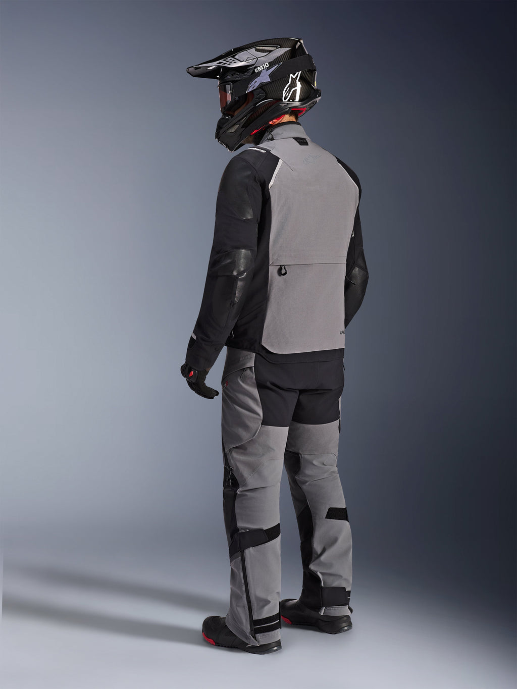 Alpinestars Andes Pro Drystar® XF-jacka, äventyrsmotorcykeljacka, mörkgrå och svart, ryggvy som visar grå ryggpanel och svarta ärmar, bärs med matchande byxor och svart hjälm, teknisk körutrustning för alla väder
