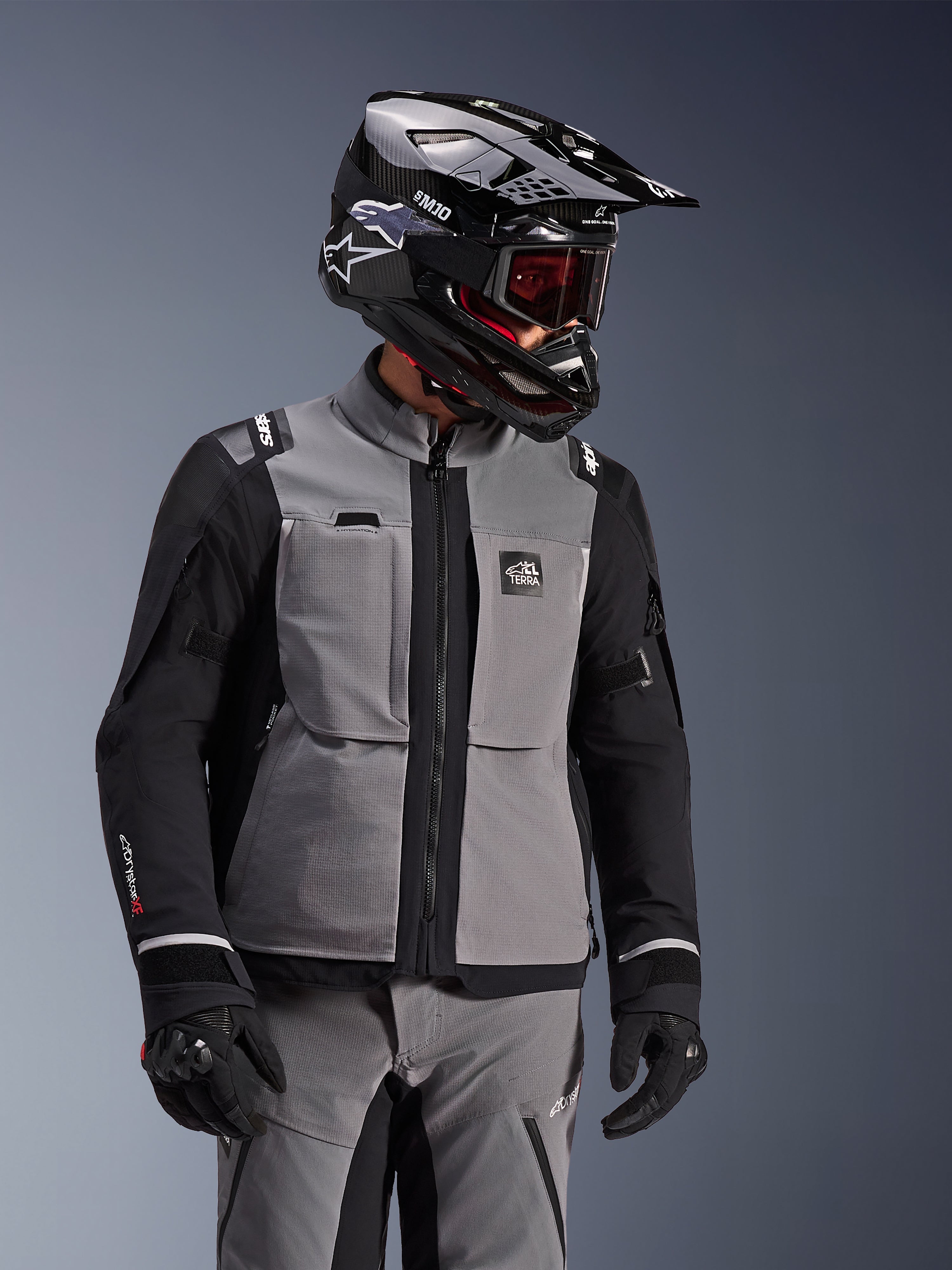 Alpinestars Andes Pro Drystar® XF-jacka, mörkgrå och svart, äventyrsmotorcykeljacka bärs med svart SM10-hjälm och matchande körutrustning, 3-lagers textildesign med central dragkedja och bröstfickor, artikulerad design för touring i alla väder