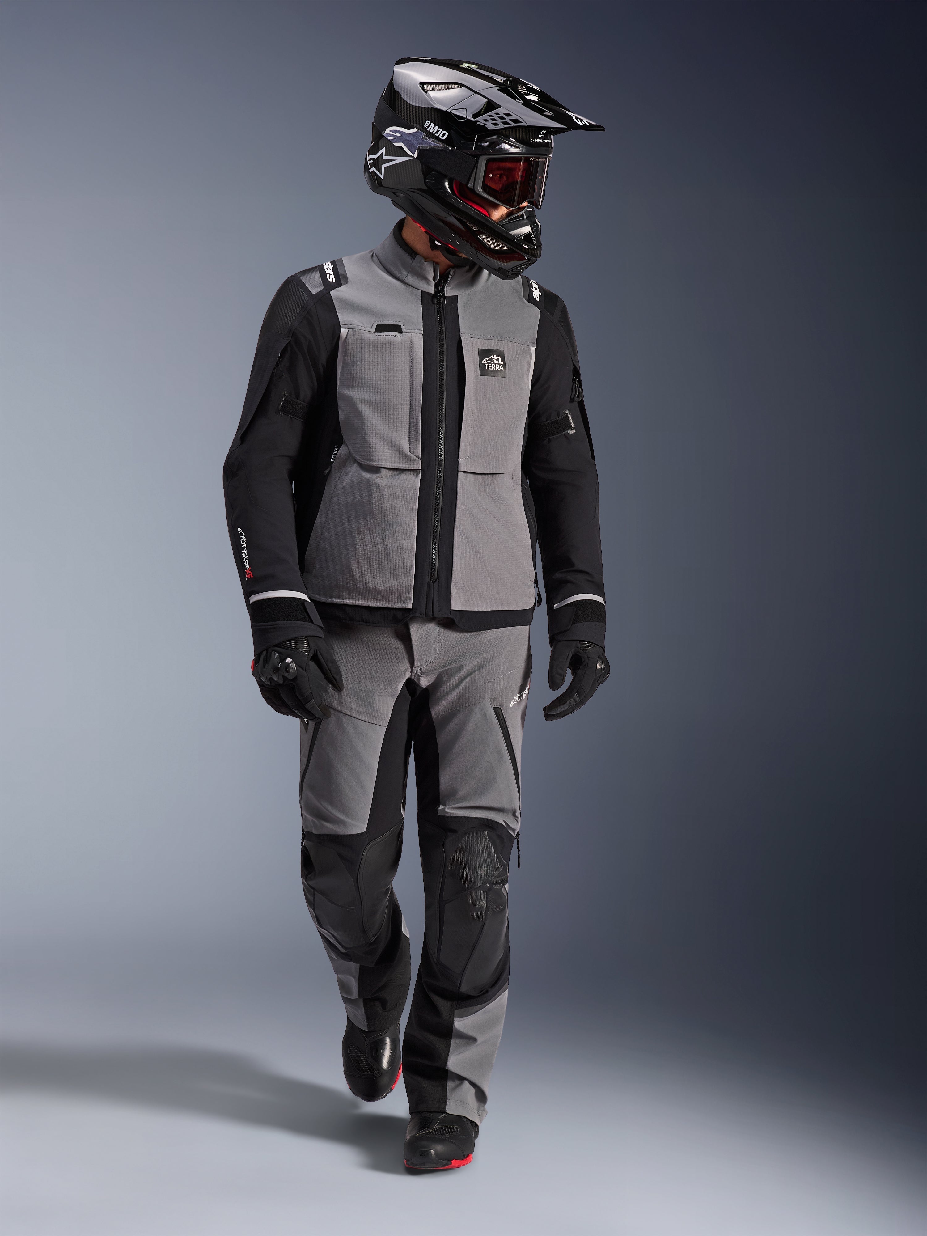 Adventure-förare iklädd Alpinestars Andes Pro Drystar® XF-jacka i mörkgrått och svart, matchande adventure-byxor, svart Alpinestars-hjälm med goggles, svarta handskar och stövlar, komplett teknisk touringutrustning för långdistanskörning