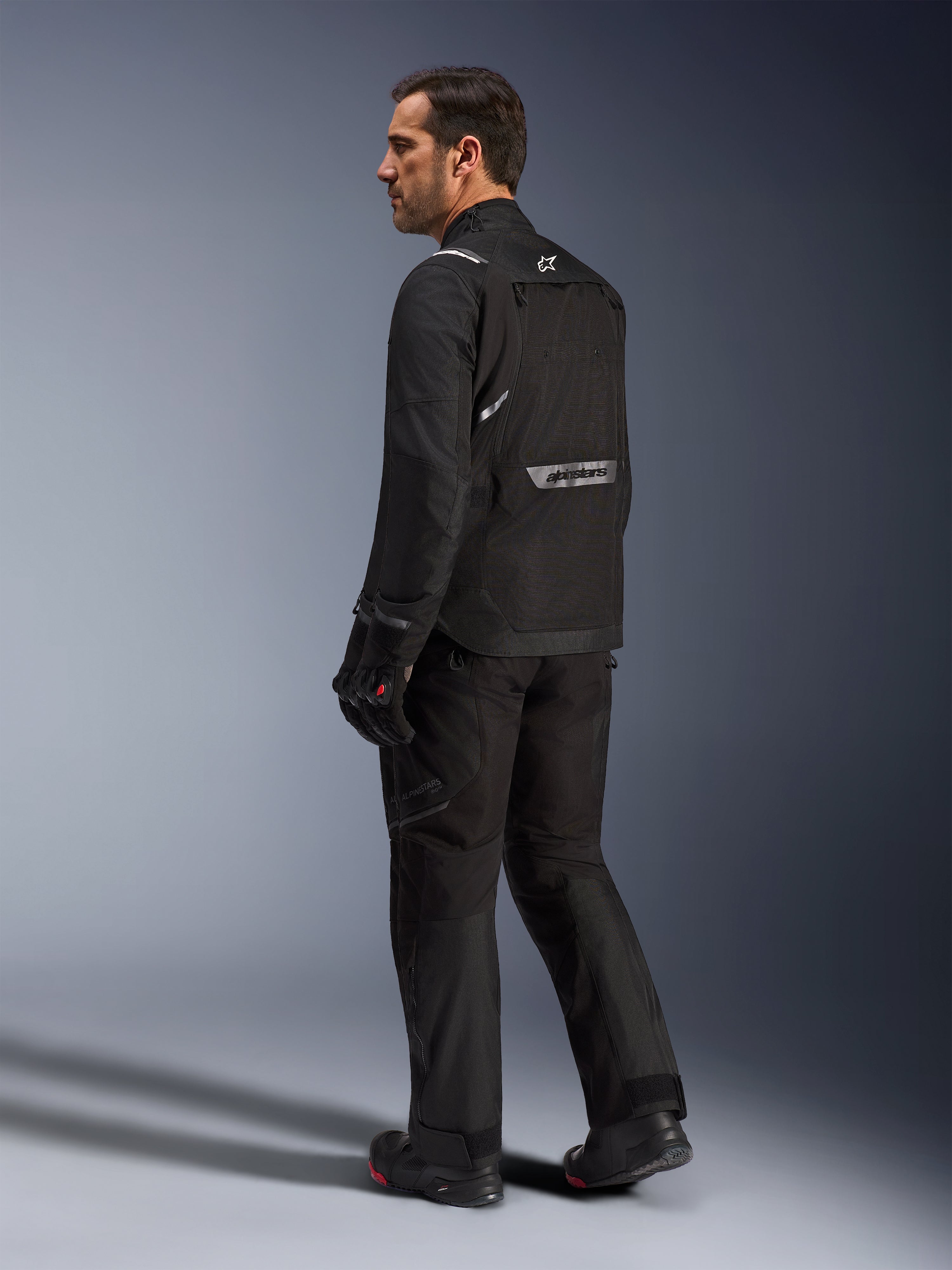 Alpinestars Cusco Drystar® Jacket, Black motorcycle jacket, back view of male model wearing full riding gear, featuring reflective branding on the back, textile construction with technical panels, coordinated outfit for road adventure touring
