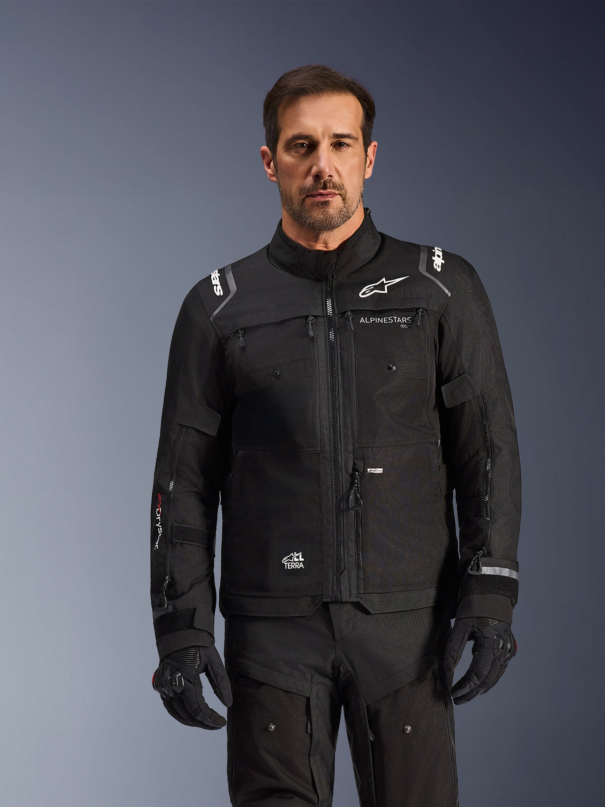 Alpinestars Cusco Drystar® jacka, svart vattentät äventyrstouringjacka i textil för herr, bärs av modell med matchande svarta handskar och byxor.