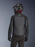 Motorcyklist sedd bakifrån bärande Alpinestars Cusco Drystar®-jacka i Black Deep Gray, med en stor grå ventilationspanel på ryggen och vit logotyp, kombinerat med en svart off-road-hjälm och svart körutrustning för äventyrstouring.