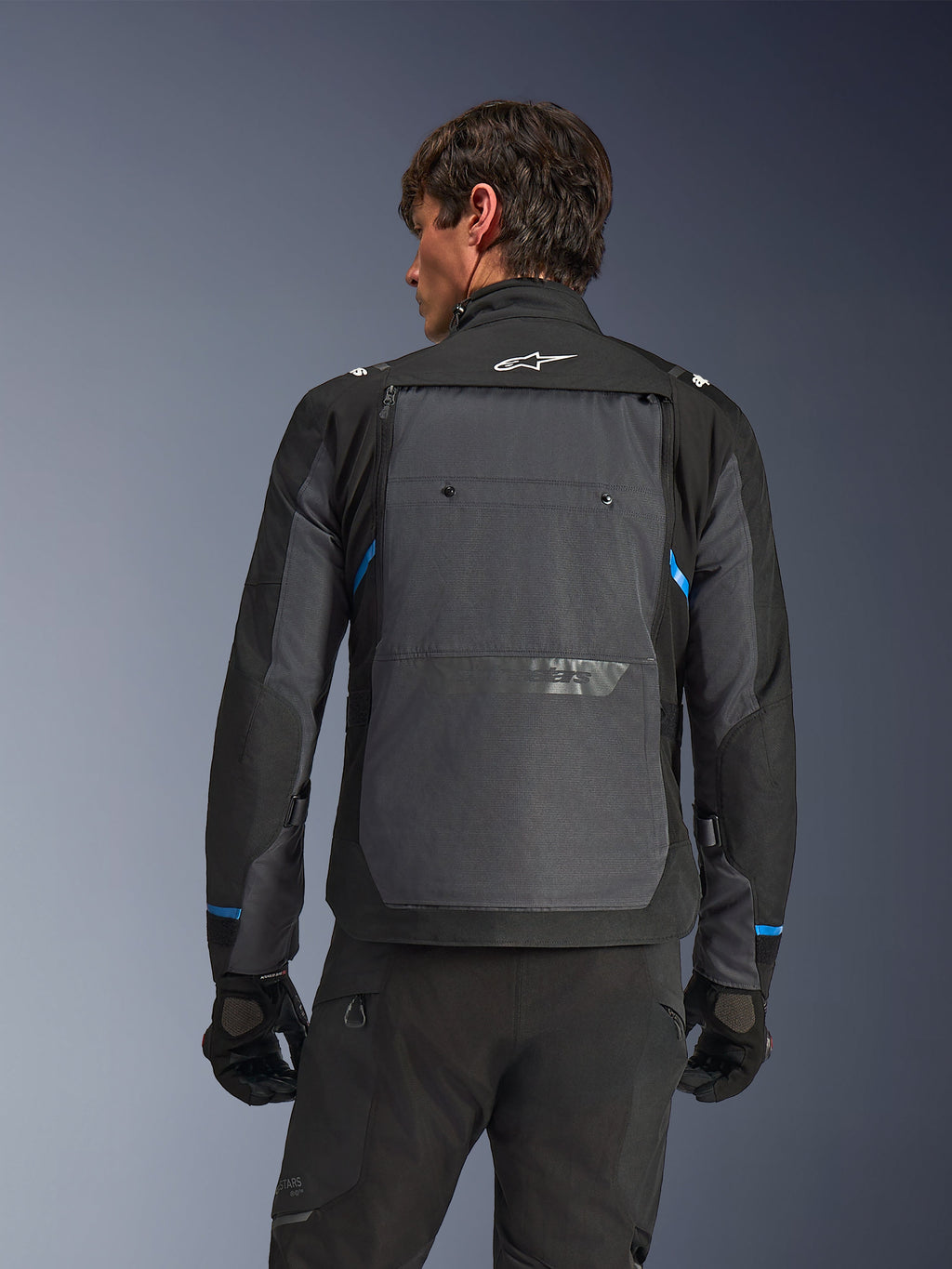 Alpinestars Cusco Drystar®-jacka, motorcykeljacka, svart och mörkgrå, ryggvy på en modell som visar en stor grå ryggpanel, vit Alpinestars-logotyp och blå detaljer på ärmarna.