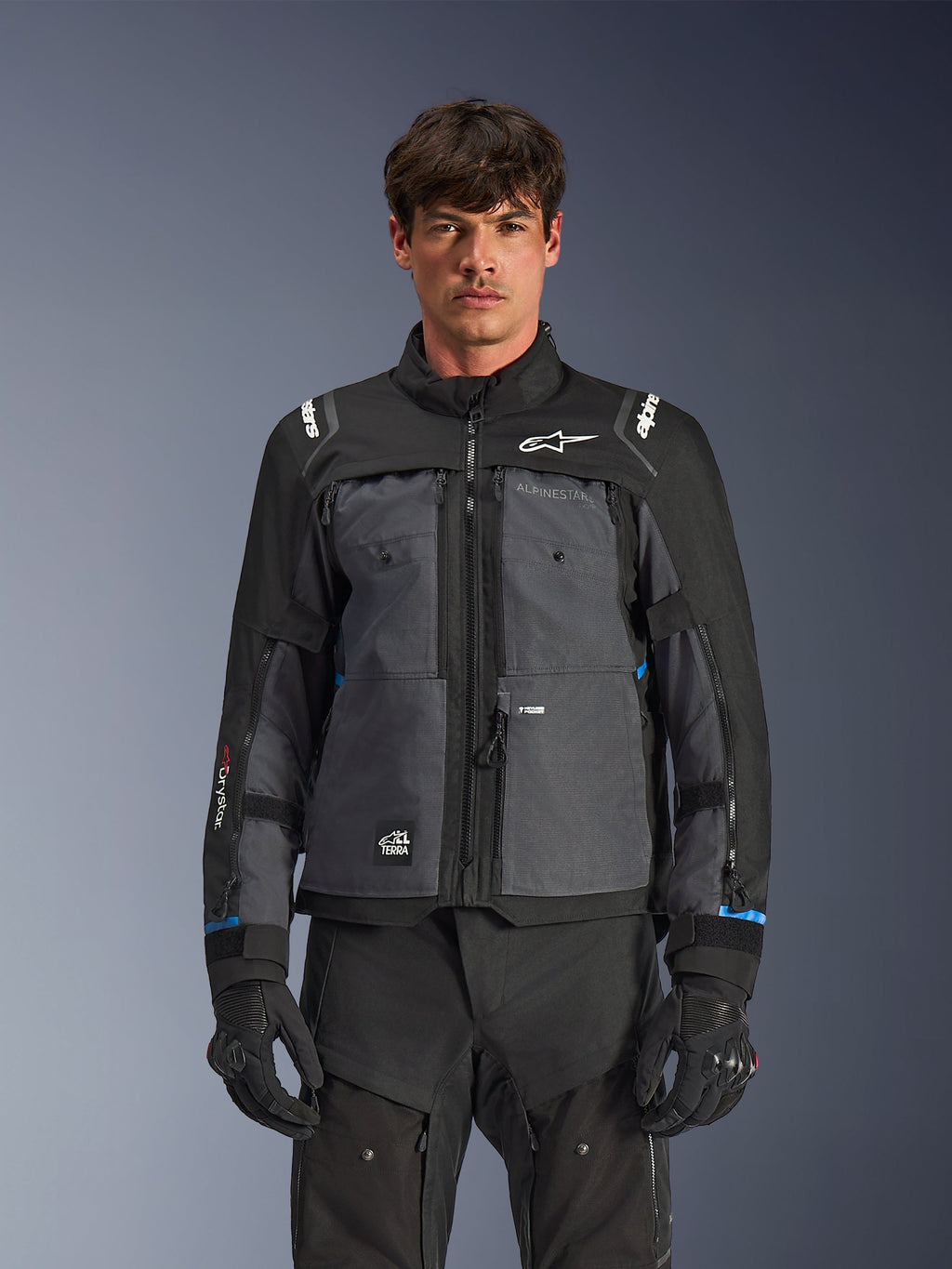 Alpinestars Cusco Drystar®-jacka, motorcykeljacka för touring, svart och mörkgrå, frontvy på modell, med Alpinestars-logotyper på bröst och axlar, Drystar®-märkning på ärmen, teknisk design med flera fickor och ventilationsdragkedjor, kombinerad med svart körutrustning