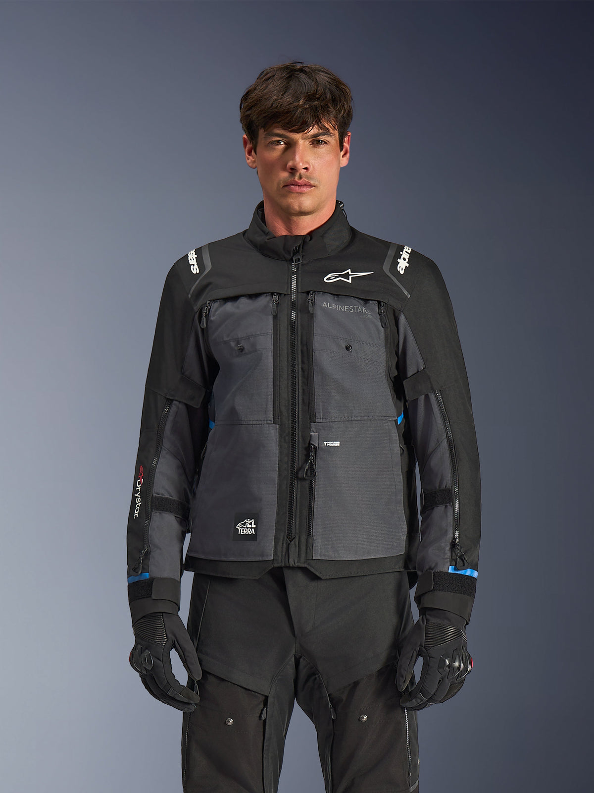 Alpinestars Cusco Drystar®-jacka, motorcykeljacka för touring, svart och mörkgrå, frontvy på modell, med Alpinestars-logotyper på bröst och axlar, Drystar®-märkning på ärmen, teknisk design med flera fickor och ventilationsdragkedjor, kombinerad med svart körutrustning