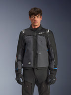 Alpinestars Cusco Drystar®-jacka, motorcykeljacka för touring, svart och mörkgrå, frontvy på modell, med Alpinestars-logotyper på bröst och axlar, Drystar®-märkning på ärmen, teknisk design med flera fickor och ventilationsdragkedjor, kombinerad med svart körutrustning