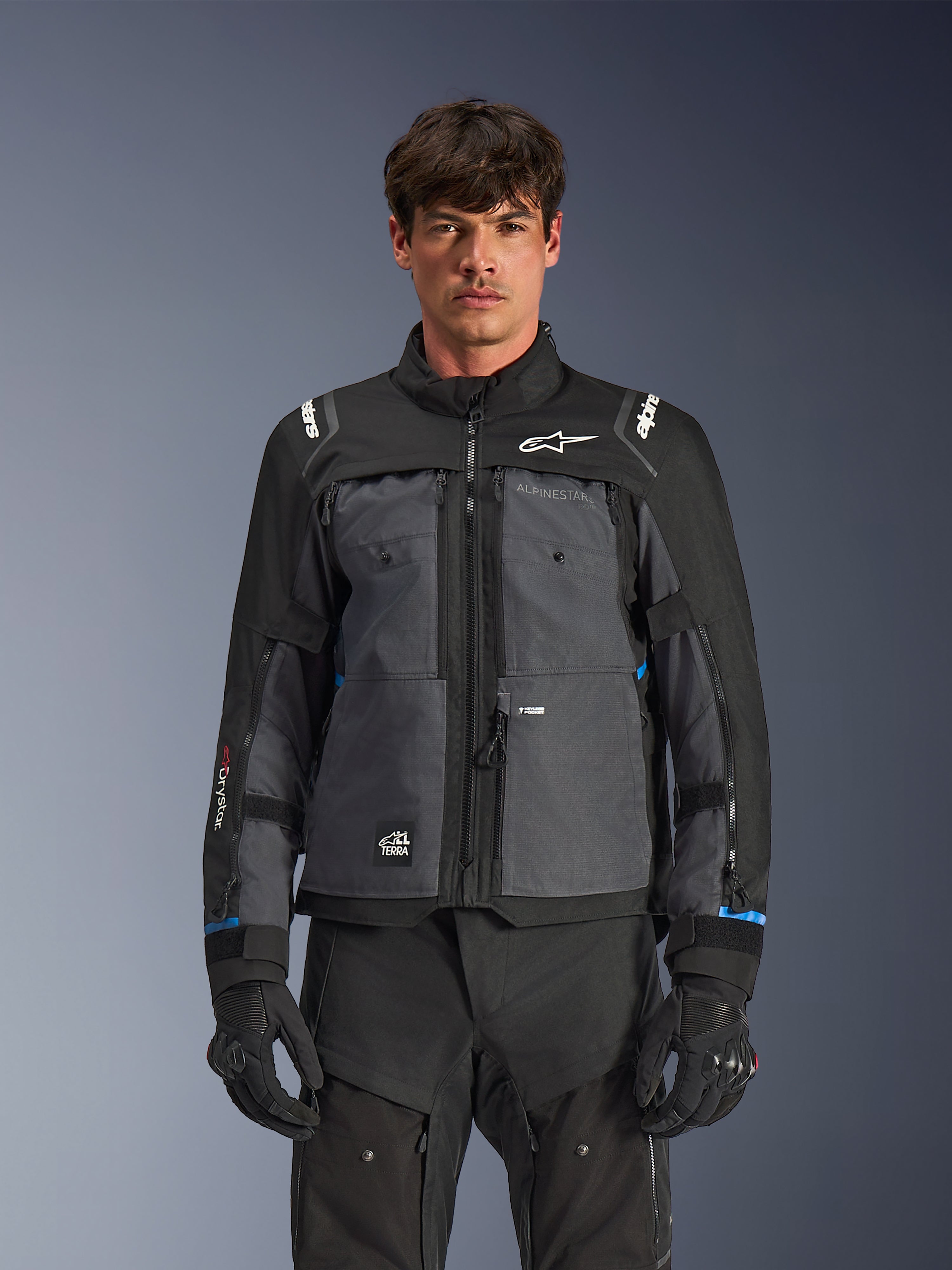 Alpinestars Cusco Drystar®-jacka, motorcykeljacka för touring, svart och mörkgrå, frontvy på modell, med Alpinestars-logotyper på bröst och axlar, Drystar®-märkning på ärmen, teknisk design med flera fickor och ventilationsdragkedjor, kombinerad med svart körutrustning