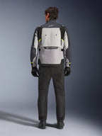 Vy bakifrån av en förare som bär Alpinestars Cusco Drystar®-jacka i Ice Gray, Mid Gray och Deep Gray, matchad med svarta motorcykelbyxor och handskar, vilket framhäver den stora ventilationspanelen på ryggen och Alpinestars logotyp.