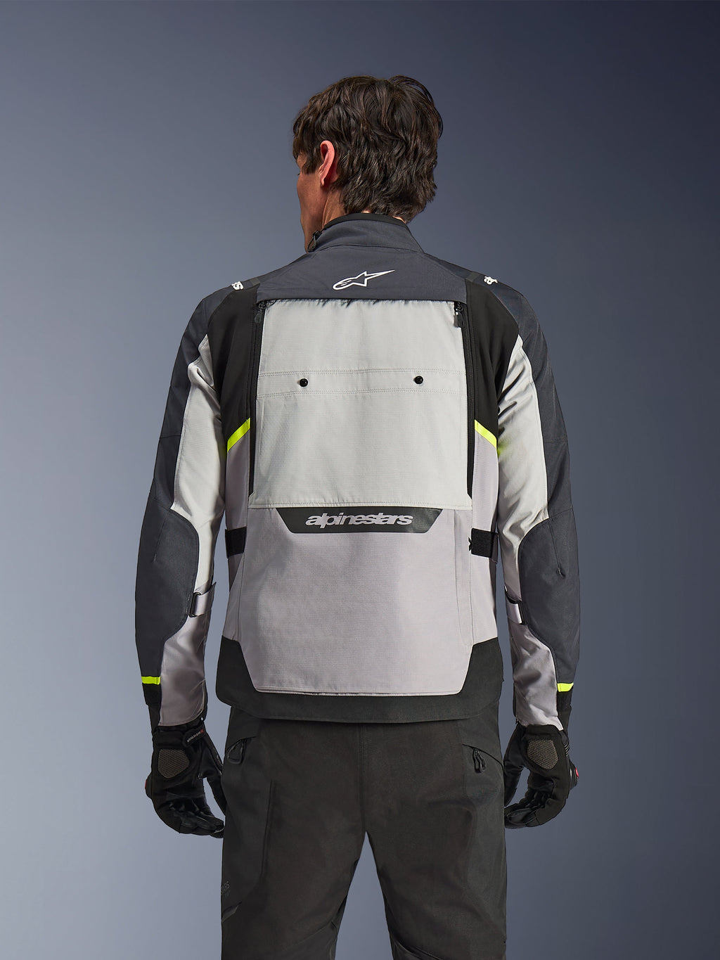 Bakifrån sedd förare som bär Alpinestars Cusco Drystar®-jacka i färgerna Ice Gray, Mid Gray och Deep Gray, med neongula accenter, en stor ventilationspanel på ryggen och tydlig Alpinestars-logotyp, matchad med svarta körbyxor och handskar.