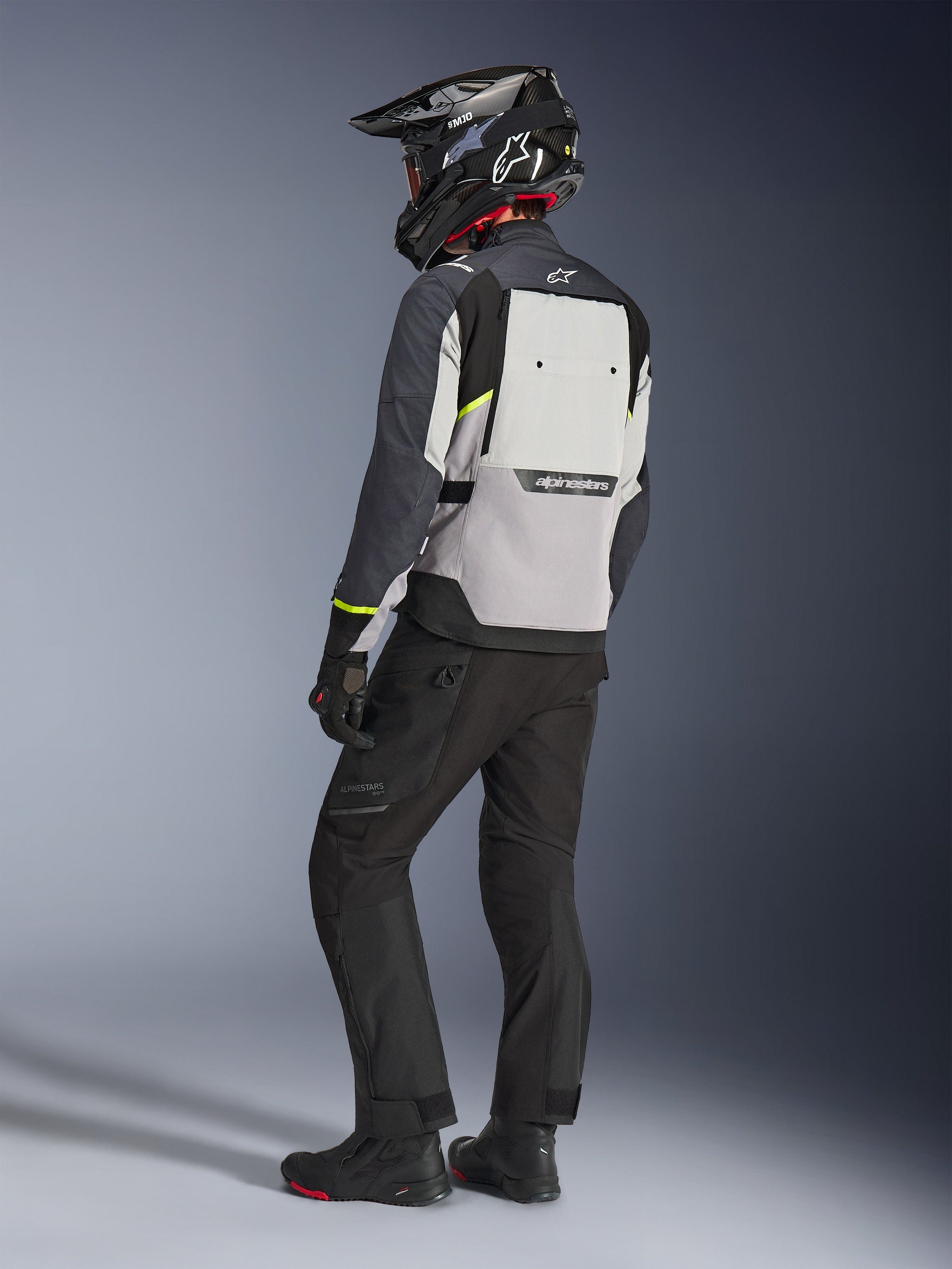 Alpinestars Cusco Drystar®-jacka i Ice Gray, Mid Gray och Deep Gray, sedd bakifrån på en förare, fluorescerande gula detaljer, stor ventilationspanel på ryggen med logotyp, hållbar textilkonstruktion, bärs med svarta motorcykelbyxor och adventure-hjälm för en komplett touring-look