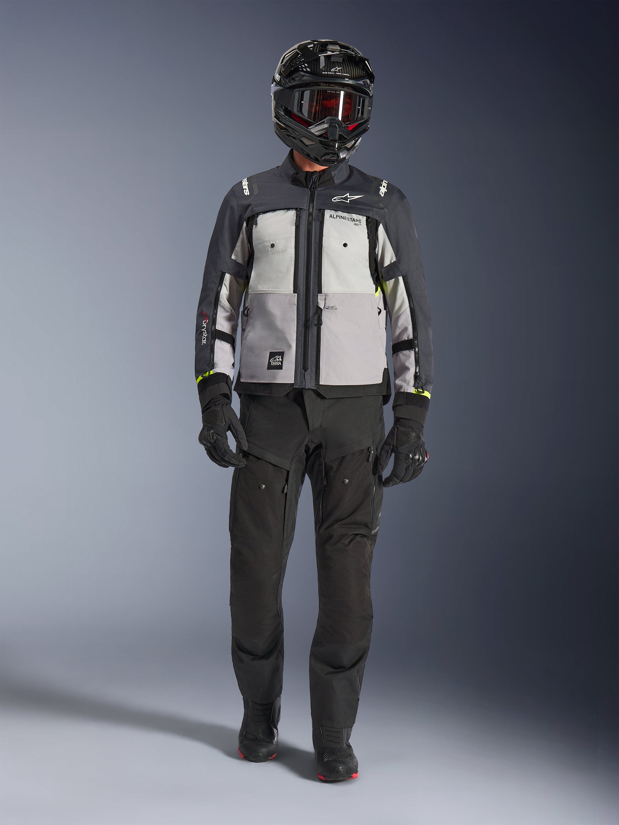 Alpinestars Cusco Drystar®-jacka, Ice Gray Mid Gray Deep Gray, äventyrsmotorcykeljacka som bärs med svarta MC-byxor, svarta handskar och en svart hjälm med goggles, med färgblockerade grå paneler och tekniska detaljer för väg- och äventyrstouring.