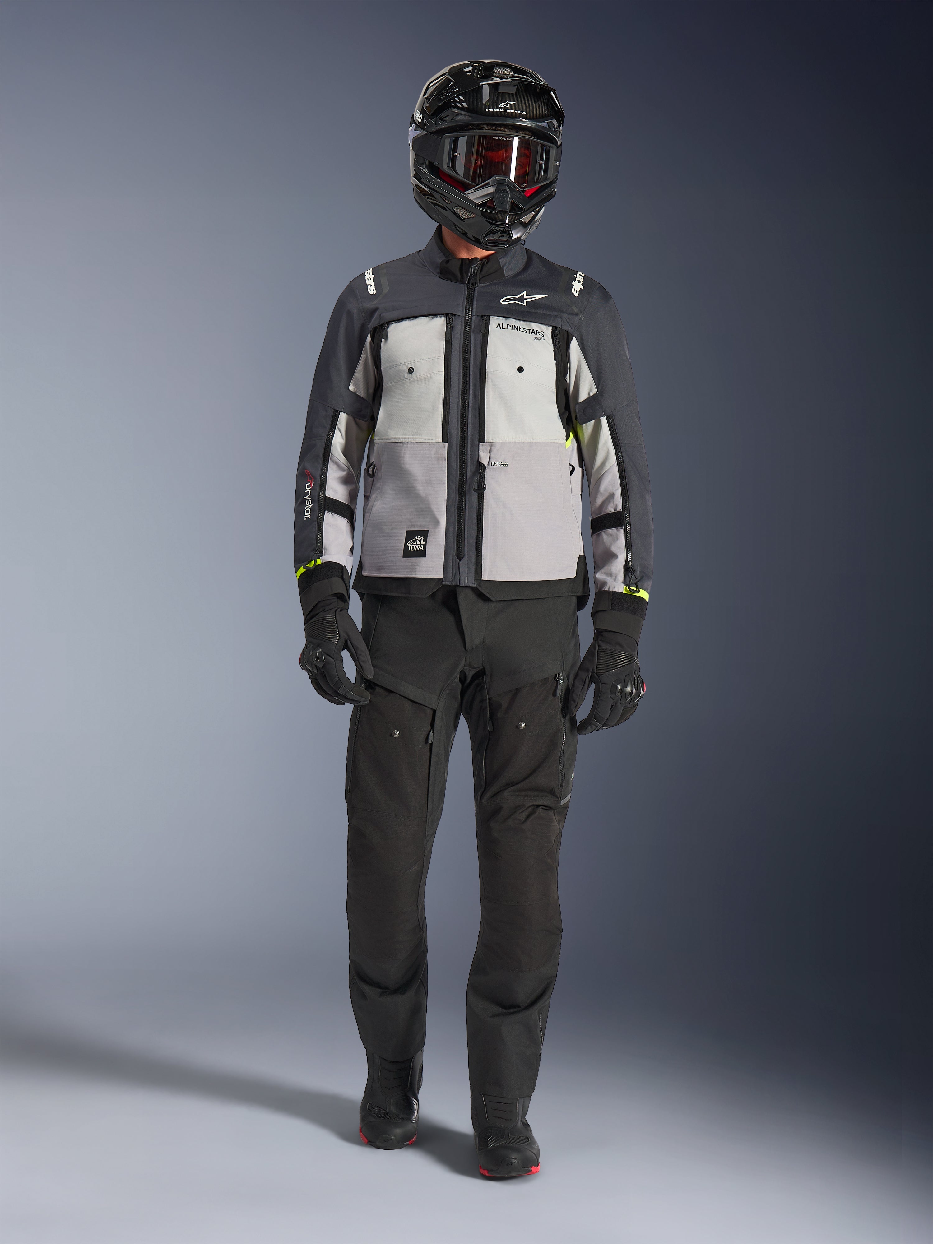 Alpinestars Cusco Drystar®-jacka, Ice Gray Mid Gray Deep Gray, äventyrsmotorcykeljacka som bärs med svarta MC-byxor, svarta handskar och en svart hjälm med goggles, med färgblockerade grå paneler och tekniska detaljer för väg- och äventyrstouring.
