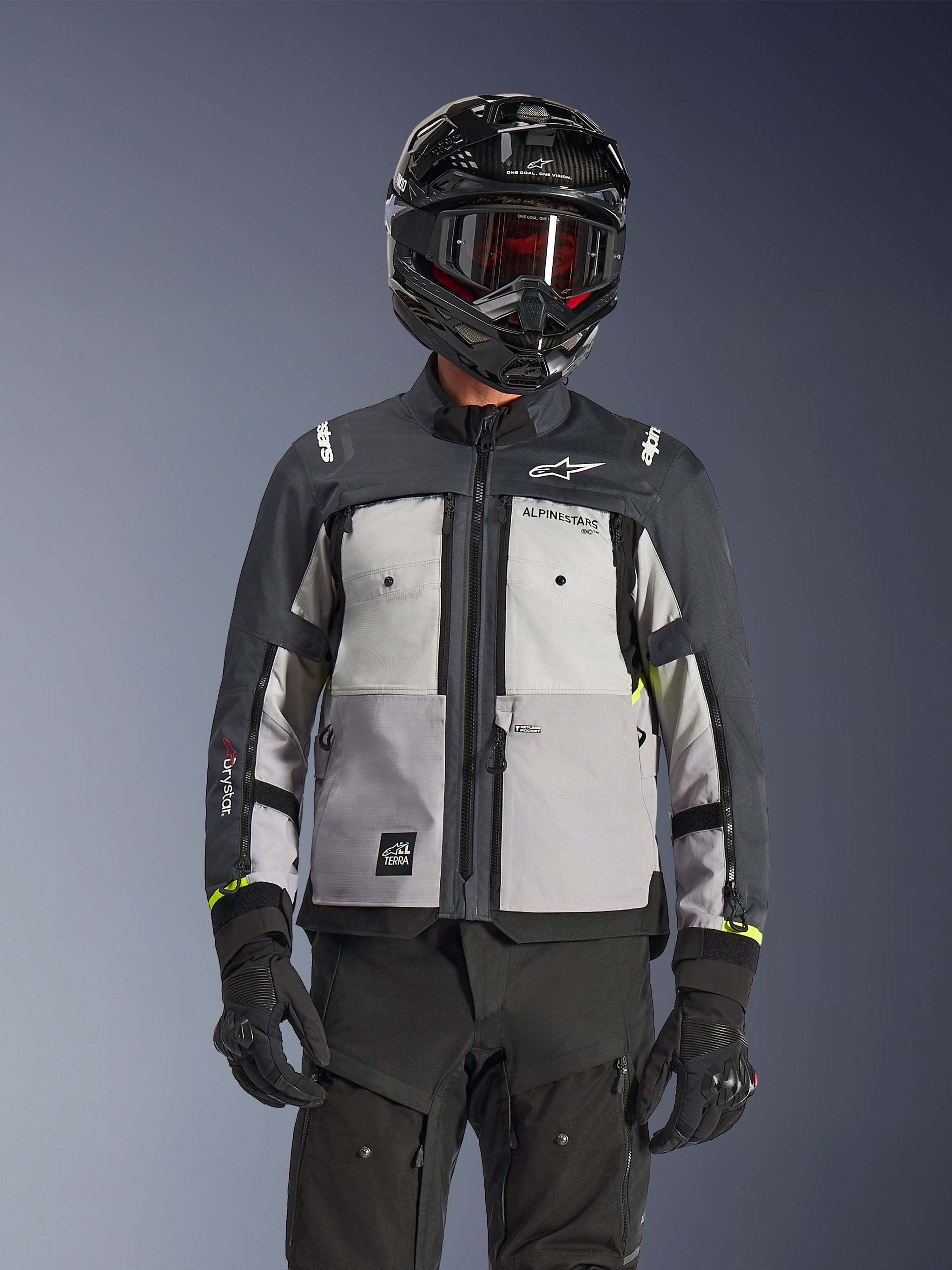 Alpinestars Cusco Drystar® jacka, äventyrsjacka, isgrå, mellangrå och djupgrå, med paneler i flera grå nyanser, ventilationsöppningar med dragkedja på bröstet och Alpinestars-logotyper, bärs av en förare med svart hjälm och goggles.