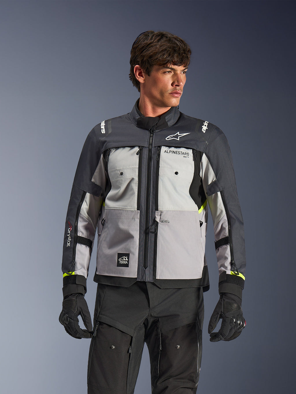 Alpinestars Cusco Drystar® jacka, adventure touring-motorcykeljacka, färgerna Ice Gray, Mid Gray och Deep Gray, bärs av en modell med svarta byxor och handskar, teknisk textildesign i flera paneler, bröstfickor, 'Drystar'-logotyp på ärmen och subtila neongula detaljer vid ärmsluten.