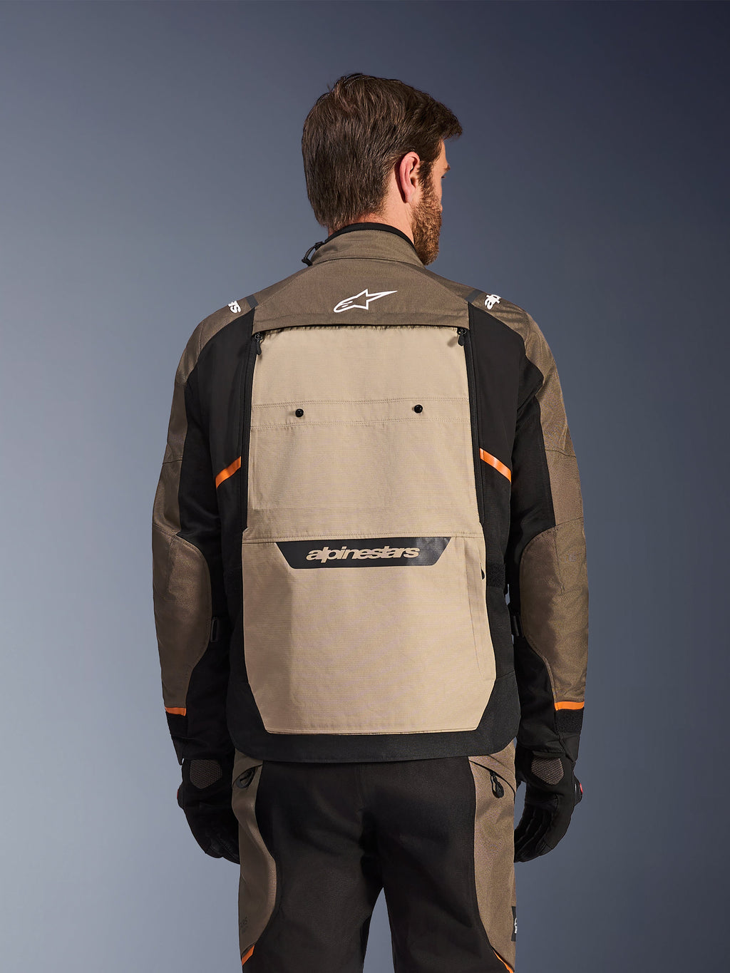 Alpinestars Cusco Drystar®-jacka, Walnut Aluminum Black, baksida, med en stor beige ryggpanel med svart logotyp, orangea detaljer, bärs med matchande byxor och handskar, designad för äventyrstouring