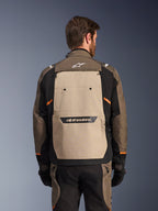 Alpinestars Cusco Drystar®-jacka, Walnut Aluminum Black, baksida, med en stor beige ryggpanel med svart logotyp, orangea detaljer, bärs med matchande byxor och handskar, designad för äventyrstouring