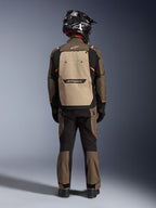 Förare sedd bakifrån i Alpinestars Cusco Drystar®-jacka i Walnut Aluminum Black, med en stor aluminiumfärgad ryggficka och orangea detaljer, matchande adventure-byxor, svart offroad-hjälm och handskar, slitstark MC-utrustning i textil för touring.