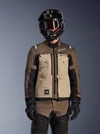 Förare i Alpinestars Cusco Drystar-jacka i Walnut Aluminum Black, MC-ställ för adventure-touring med svart hjälm, goggles och svarta handskar, framifrån som visar teknisk textilkonstruktion, fickor och logotyper.