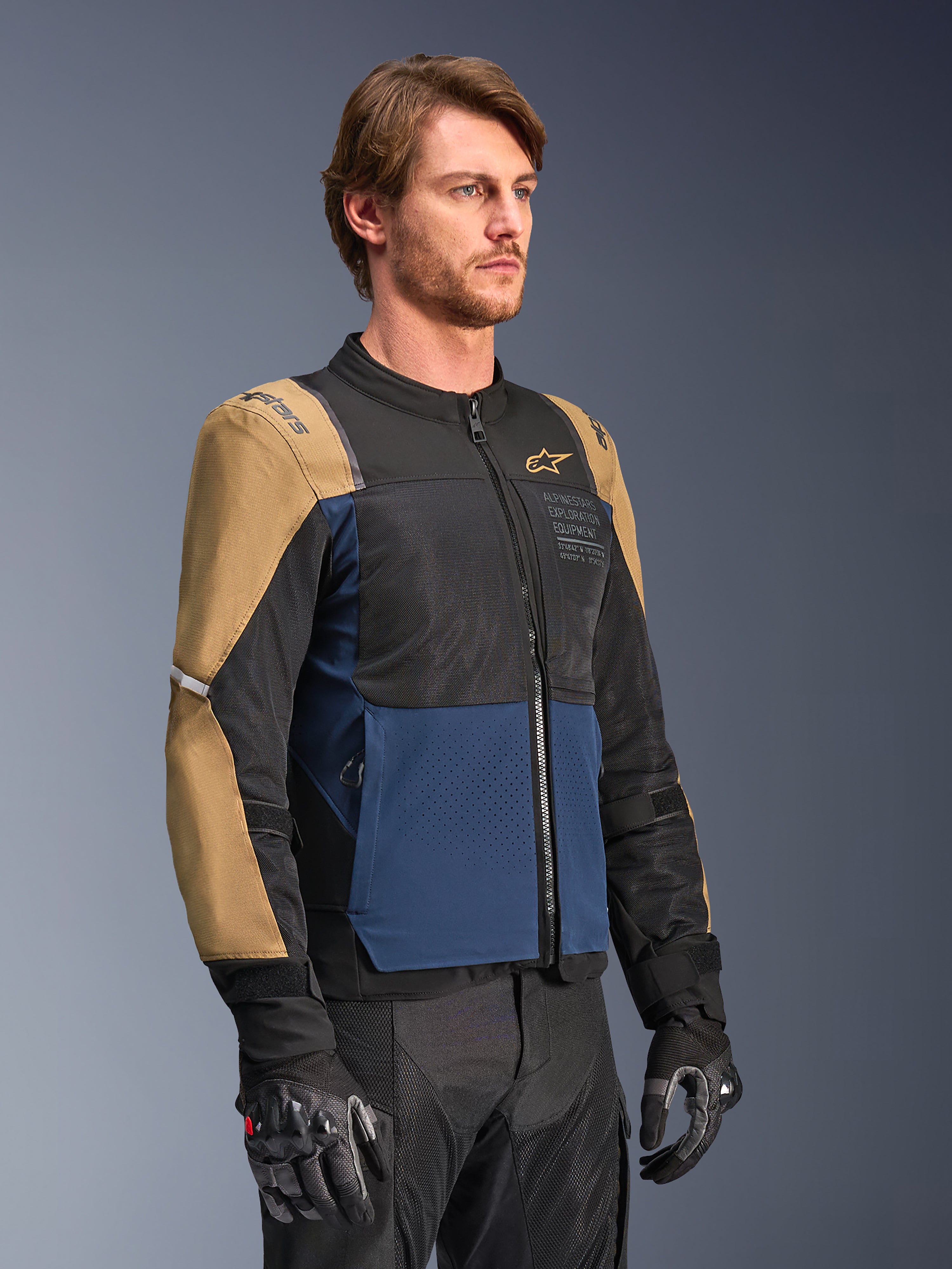 Alpinestars ST-2 Air Jacka, motorcykeljacka, mörkblå, mörk khaki och svart, med meshpaneler för högt luftflöde och 'Alpinestars Exploration Equipment'-märkning, bärs med svarta körhandskar, modern adventure touring-design