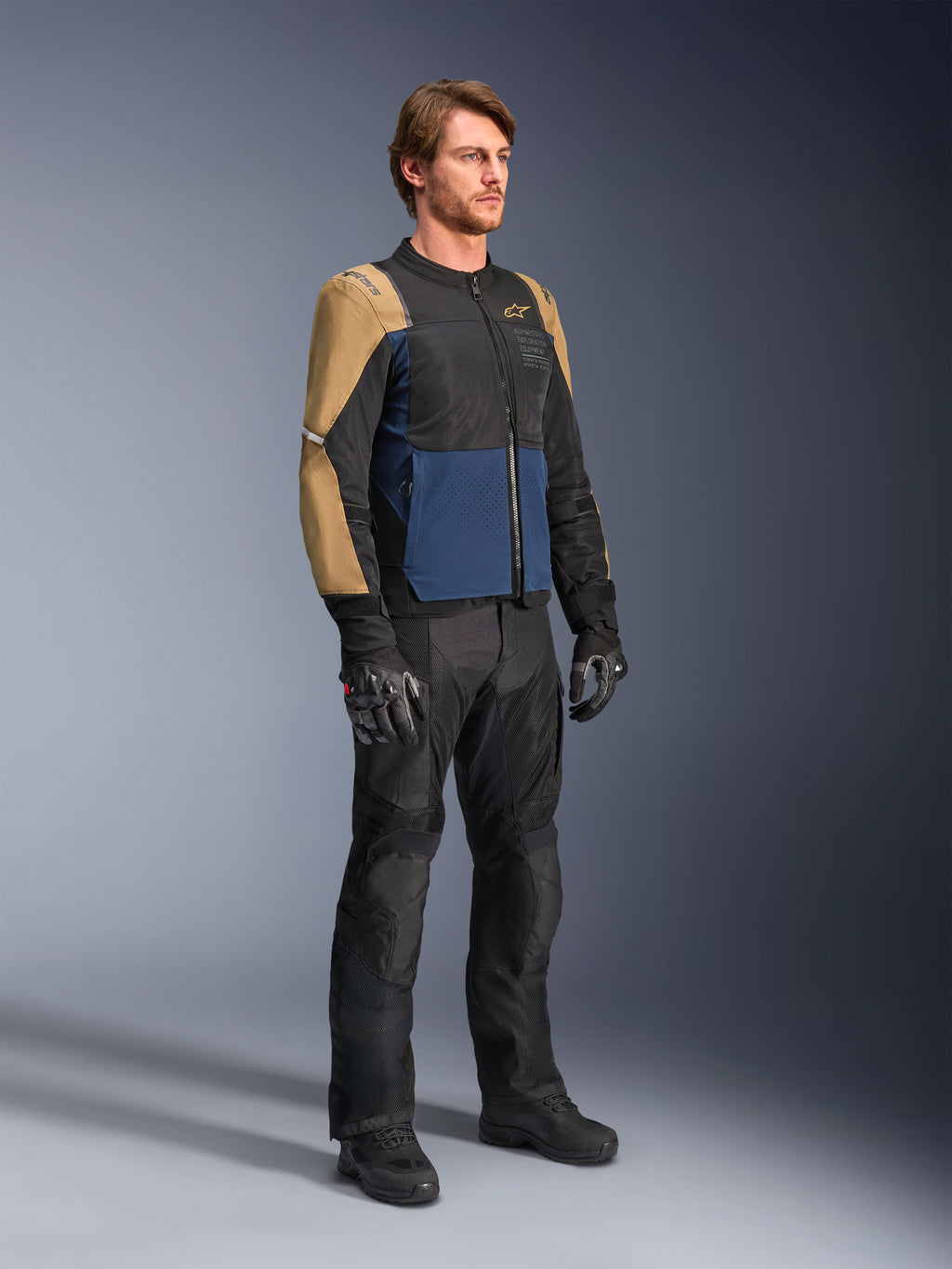 Manlig mc-förare klädd i Alpinestars ST-2 Air-jacka i färgerna Deep Blue, Dark Khaki och svart, med stora meshpaneler och laserperforeringar, kombinerat med svarta motorcykelbyxor, handskar och stövlar för en komplett touring-look för sommaren.
