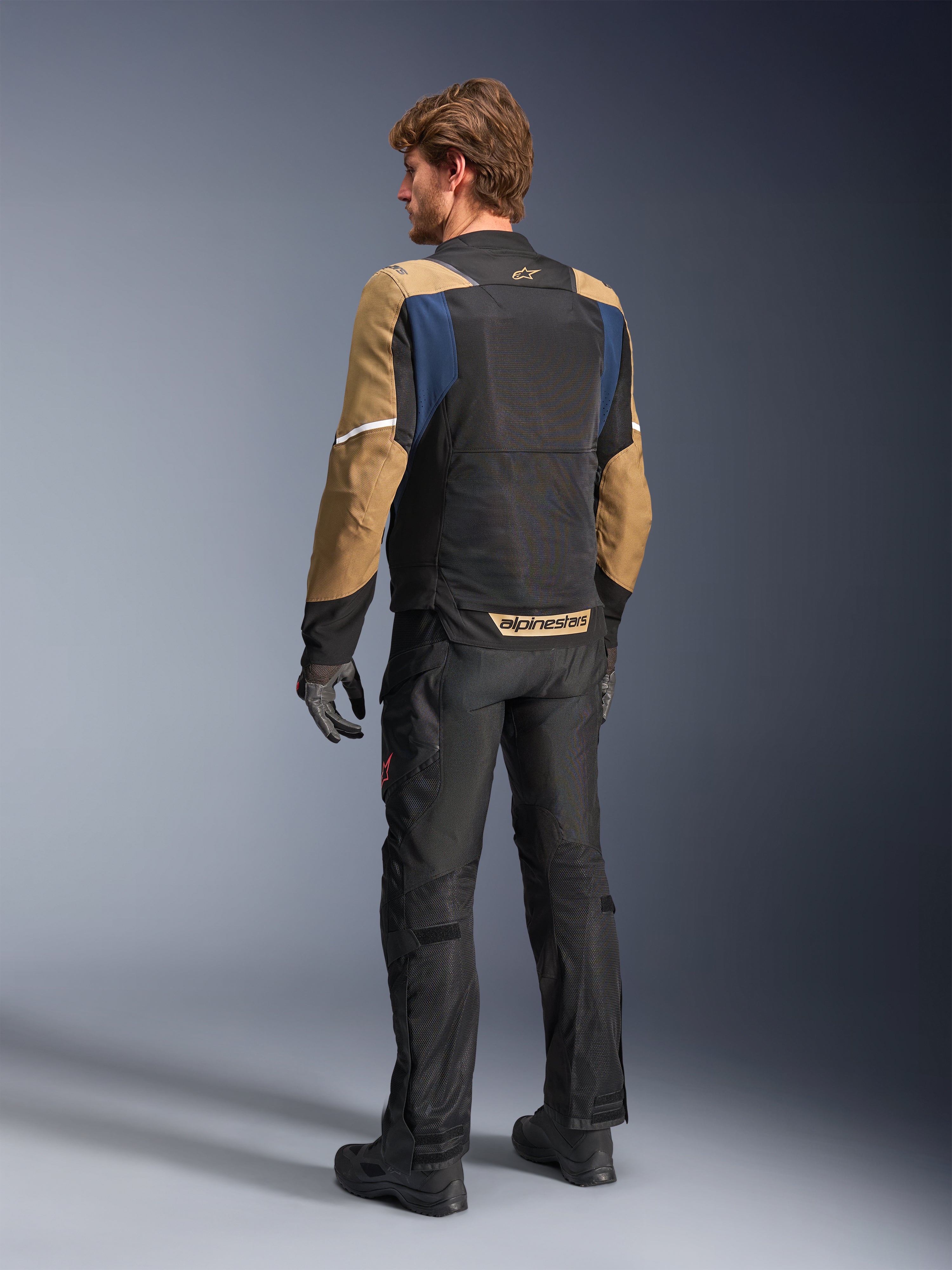 Alpinestars ST-2 Air Jacket, sommartouringjacka för motorcykel, Deep Blue, Dark Khaki och svart, vy bakifrån på modell som visar meshpaneler, khakifärgade ärmar och blå accenter, med vita reflexband och tydlig logotyp på nedre ryggen, kombinerad med svarta motorcykelbyxor