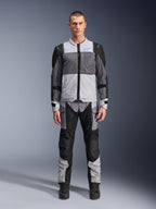Alpinestars ST-2 Air jacka, touringjacka för motorcykel, Ice Gray, mörkgrå och svart, bärs av en modell med matchande adventure-byxor, stora meshpaneler, blå Alpinestars-logotyp på bröstet och Alpinestars Exploration Equipment-märkning