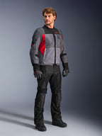 Male model wearing Alpinestars ST-2 Air Jacket, Textile Motorcycle Jacket, Deep Gray Dark Gray and Bright Red, paired with black pants, gloves and boots, featuring large mesh panels, Alpinestars Exploration Equipment branding, and a modern touring aesthetic