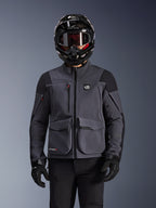 Alpinestars Maxdura Drystar®XF Laminated Armored Shell, motorcykeljacka, mörkgrå och svart, bärs av en förare med svart hjälm, goggles och handskar, med stora tekniska cargofickor och ALL TERRA-märkning, adventure touring-utrustning
