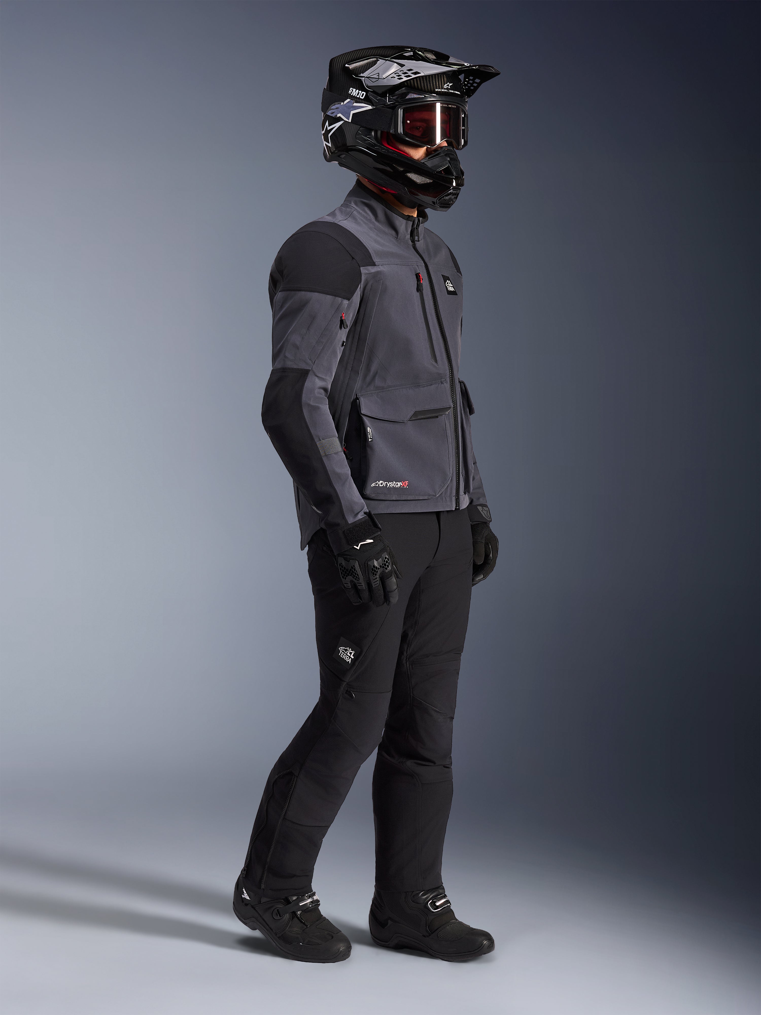 Motorcykelförare i Alpinestars Maxdura Drystar®XF Laminated Armored Shell-jacka i Deep Gray och svart, kombinerad med svarta adventure-byxor, svart hjälm med goggles, svarta handskar och stövlar, studiobild i helfigur som framhäver den tekniska dual-sport-utrustningen.