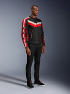 Manlig modell i Alpinestars T-Dyno WR-jacka, textilmotorcykeljacka i Black Bright Red Ecru, med röda och off-white ränder och Alpinestars stjärnlogotyper på ärmarna, matchad med svarta byxor och svarta höga sneakers, vintageinspirerad urban MC-utrustning.