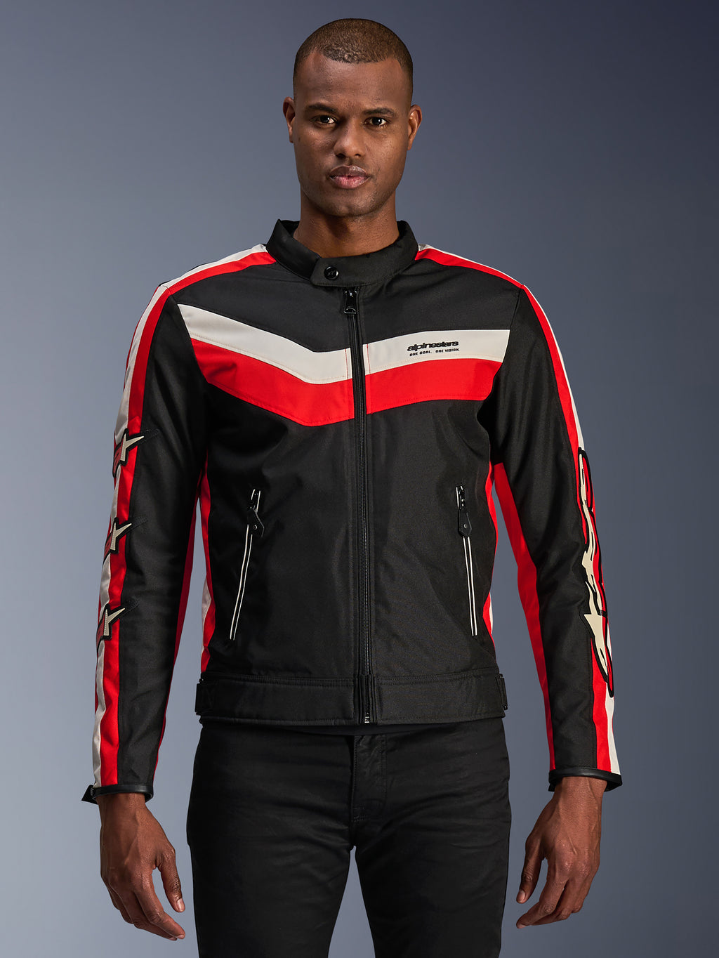 Alpinestars T-Dyno WR-jacka, motorcykeljacka i textil, svart med klarröda och ecruvita chevronränder, vintageinspirerad biker-passform, hög krage med knappstängning, framfickor med dragkedja, stjärnlogotyper på ärmarna, bärs av modell