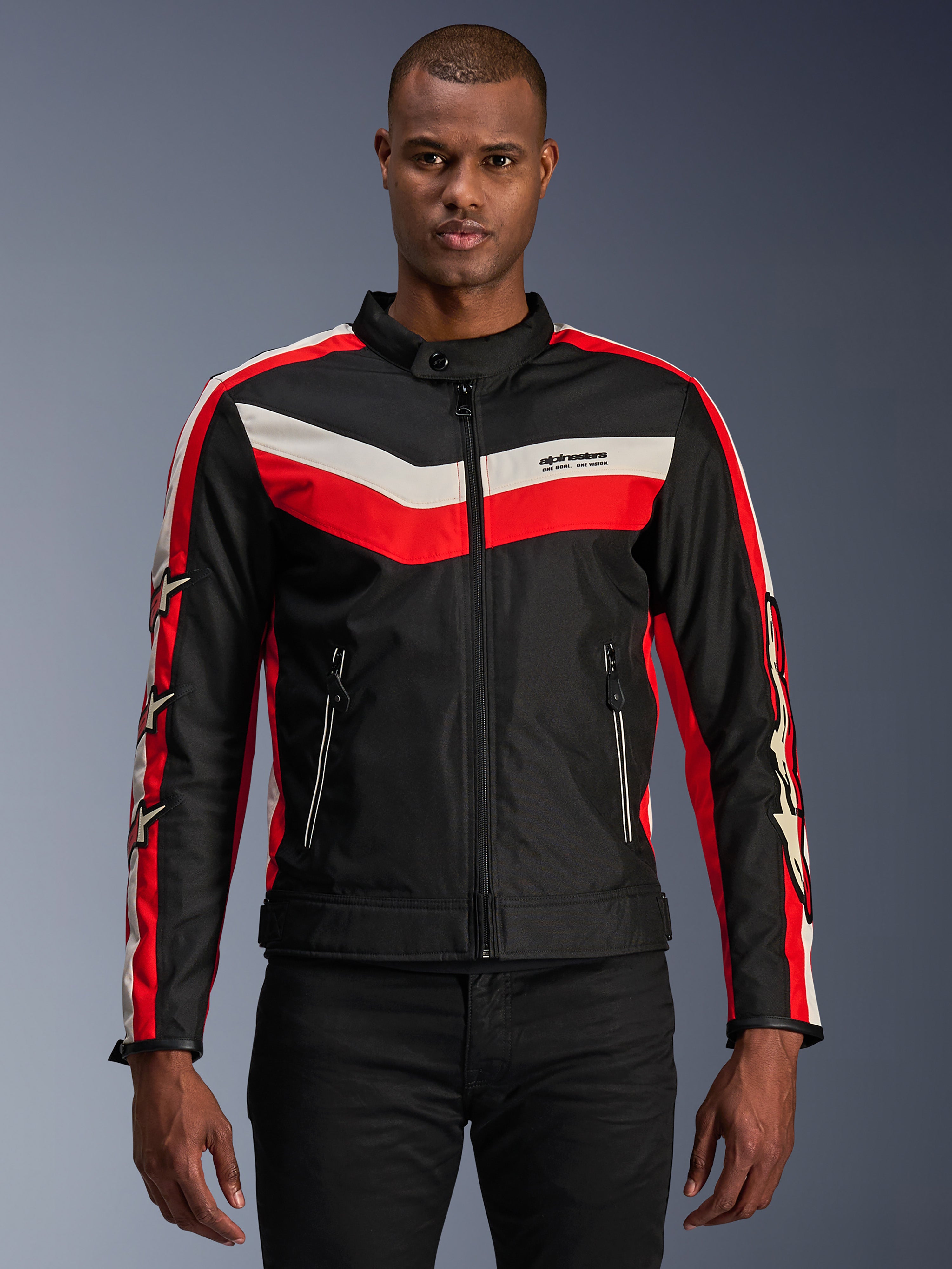 Alpinestars T-Dyno WR-jacka, motorcykeljacka i textil, svart med klarröda och ecruvita chevronränder, vintageinspirerad biker-passform, hög krage med knappstängning, framfickor med dragkedja, stjärnlogotyper på ärmarna, bärs av modell