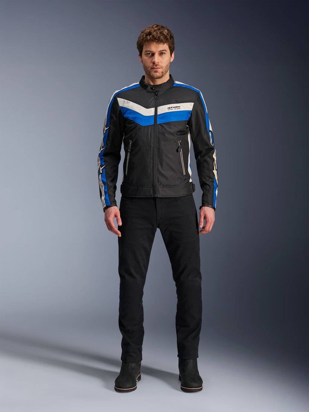 Alpinestars T-Dyno WR-jacka, textiljacka för motorcykel, svart, blå och ecru, bärs av en manlig modell med svarta byxor och stövlar, med chevron-ränder på bröstet och klassisk bikerdesign