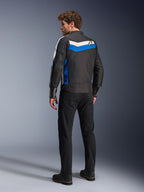 Alpinestars T-Dyno WR-jacka i Black Blue Ecru, sedd bakifrån på en manlig modell, med en vit och blå chevron-rand över axlarna och en stjärnlogotyp, vintageinspirerad textilmotorcykeljacka, bärs med svarta byxor och stövlar