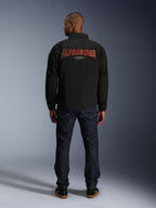 Alpinestars Revved WR Jacket, Black, back view featuring large red 3D-effect 'ALPINESTARS' embroidery, urban coaches-style jacket, worn with dark denim jeans and black sneakers, minimalist motorcycle apparel
