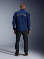 Alpinestars Revved WR-jacka i marinblått, sedd bakifrån, med ett stort "ALPINESTARS"-broderi med 3D-effekt över ryggen, stylad med mörka denimjeans och svarta sneakers, urban motorcykelutrustning.