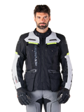 Man som bär Alpinestars Bogotá Pro Drystar®-jacka i färgerna svart, isgrå och neongul, allväders motorcykeljacka för adventure-touring, vattentät design med flera fickor och vertikal logotyp, matchad med svarta handskar och grå körbyxor